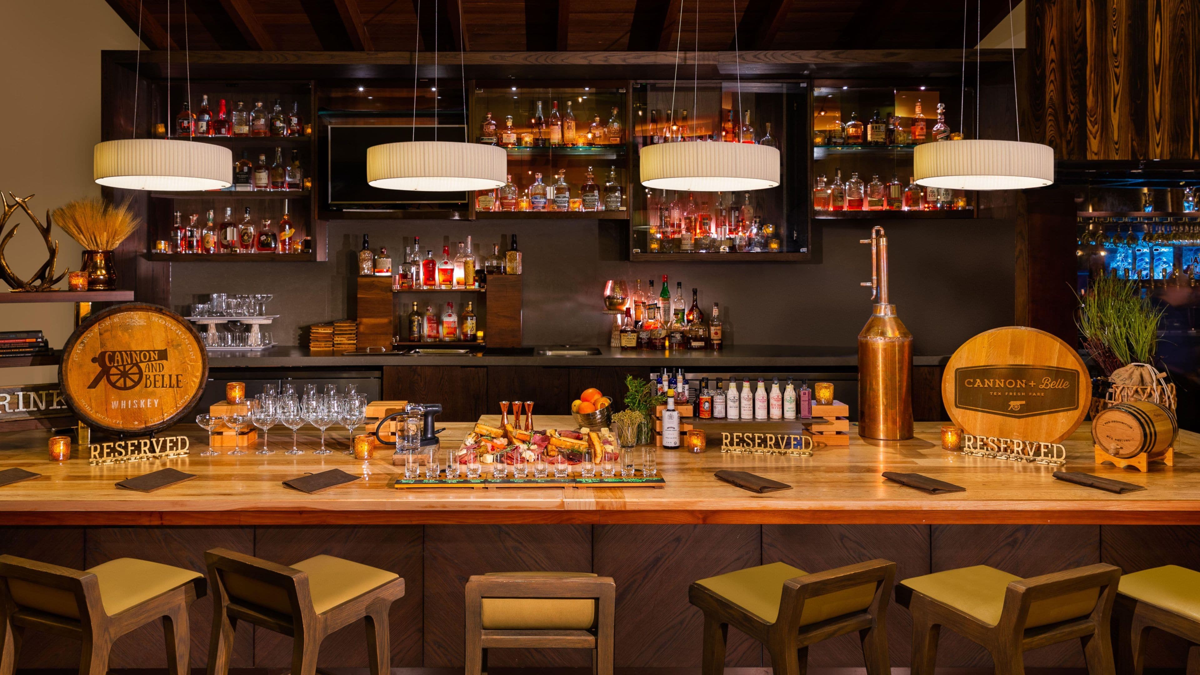 Un bar con varias botellas de licor, un barril de whisky y un alambique de cobre. Hay taburetes de bar y un cartel que indica que el bar está reservado.