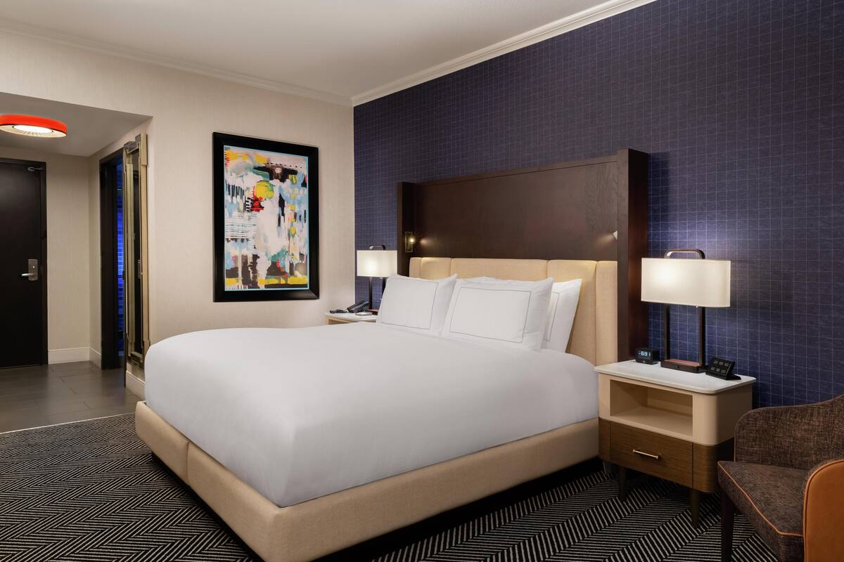 A hotel room with a large bed, two bedside tables with lamps, a framed picture on the wall, and a patterned carpet.