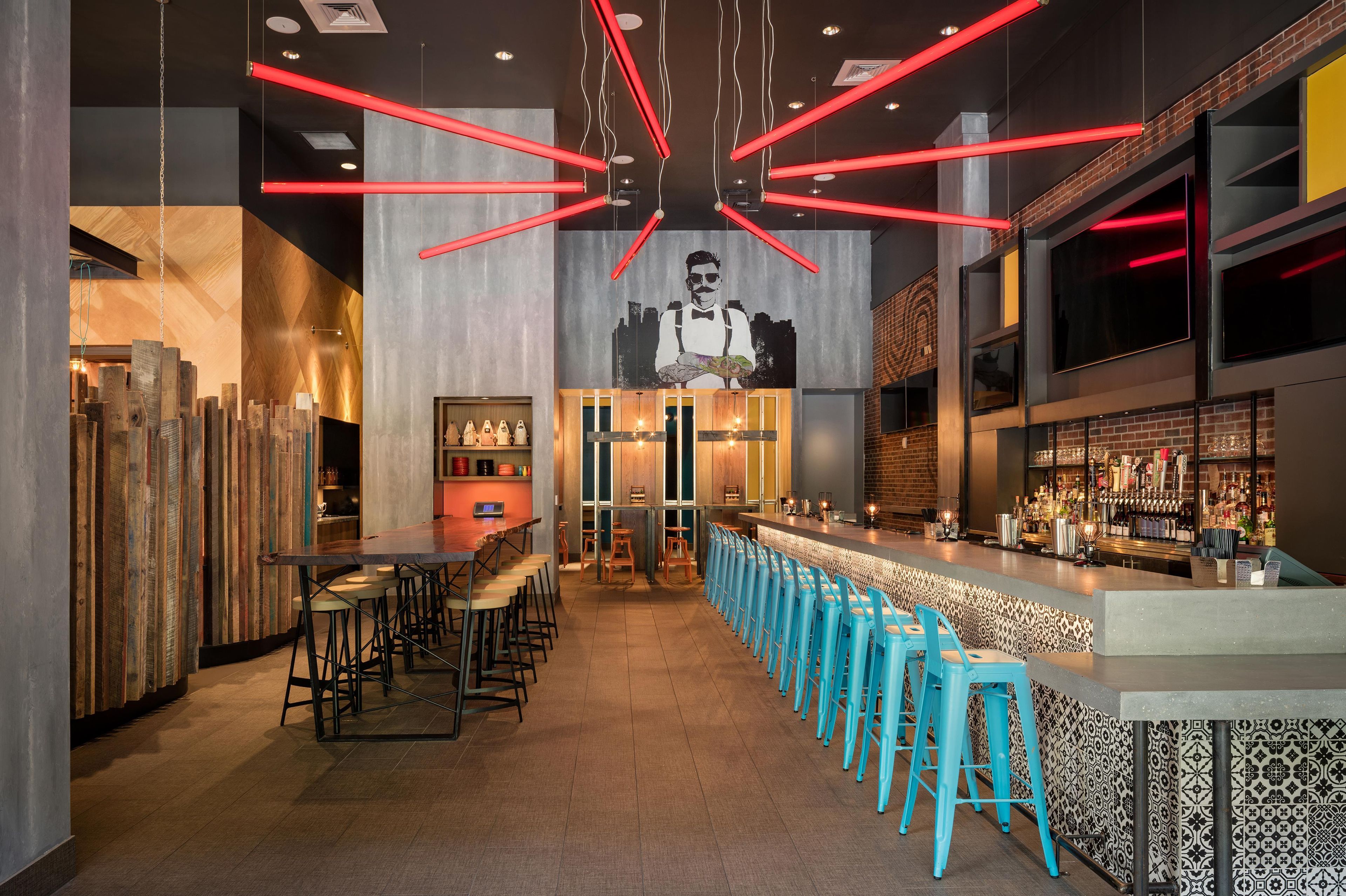 Un espace bar avec un long comptoir, des tabourets de bar bleus et une fresque murale.