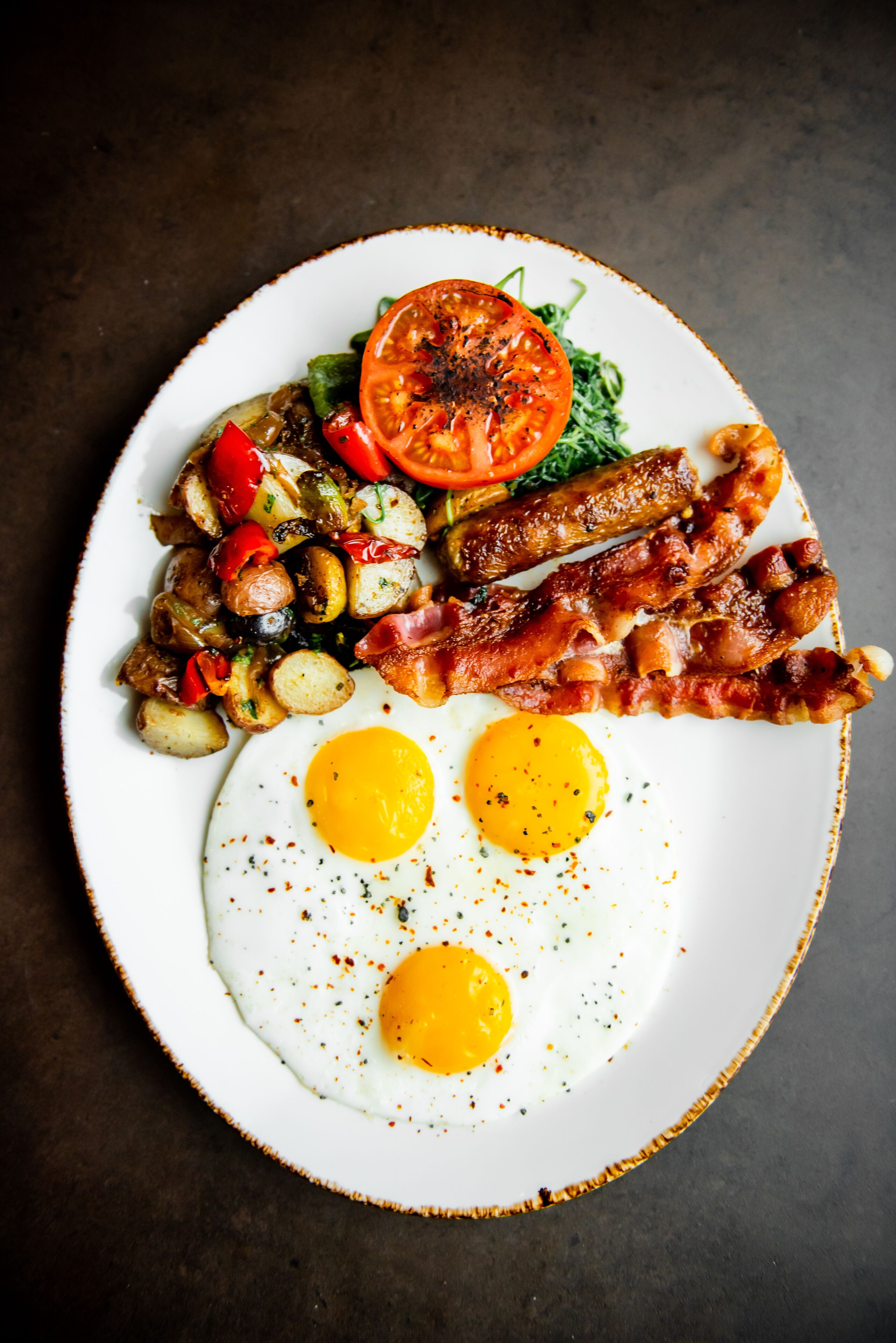 Prato de comida de café da manhã com ovos, bacon, linguiça e legumes.