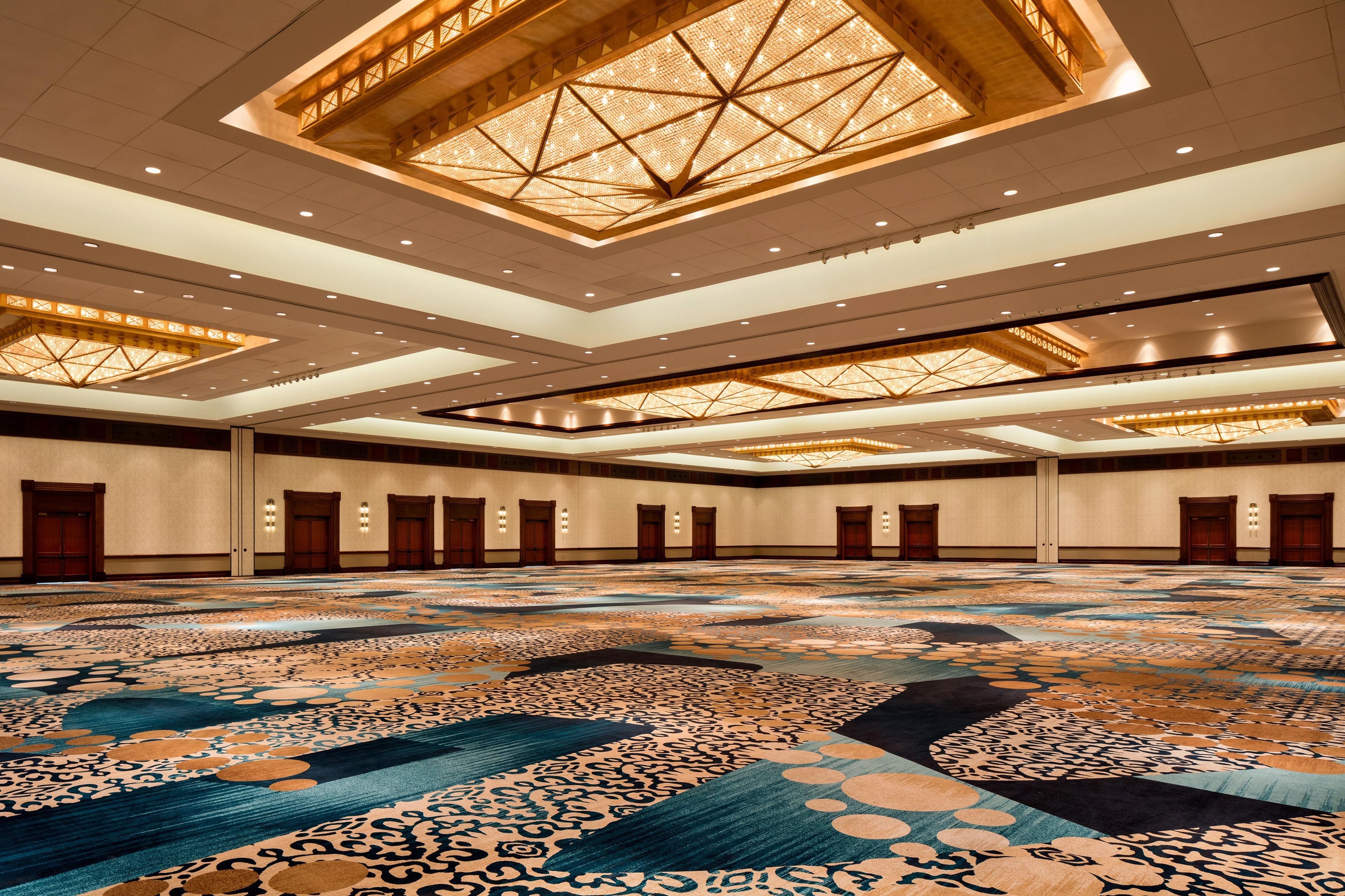 Un hall d’hôtel spacieux, doté d’un plafond haut, d’un tapis à motifs et de plusieurs portes.