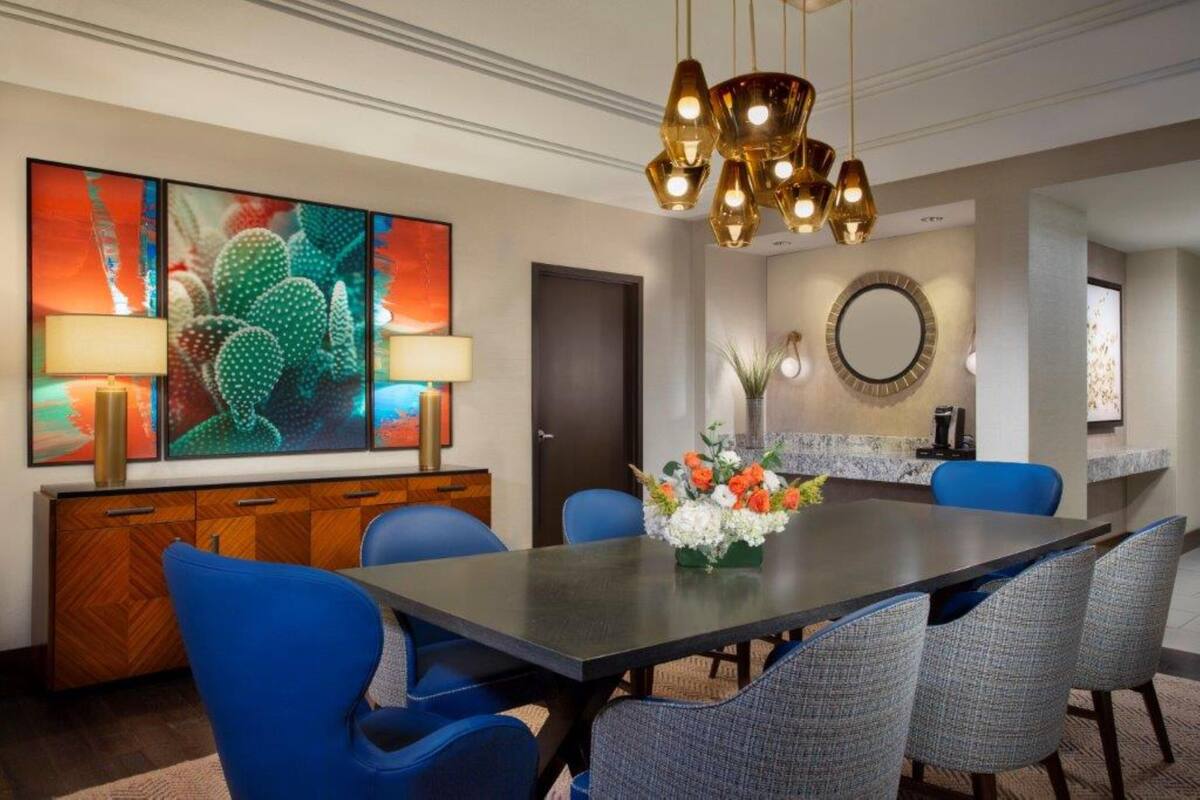 A dining area with a long table, blue chairs, a decorative vase, and a modern chandelier.