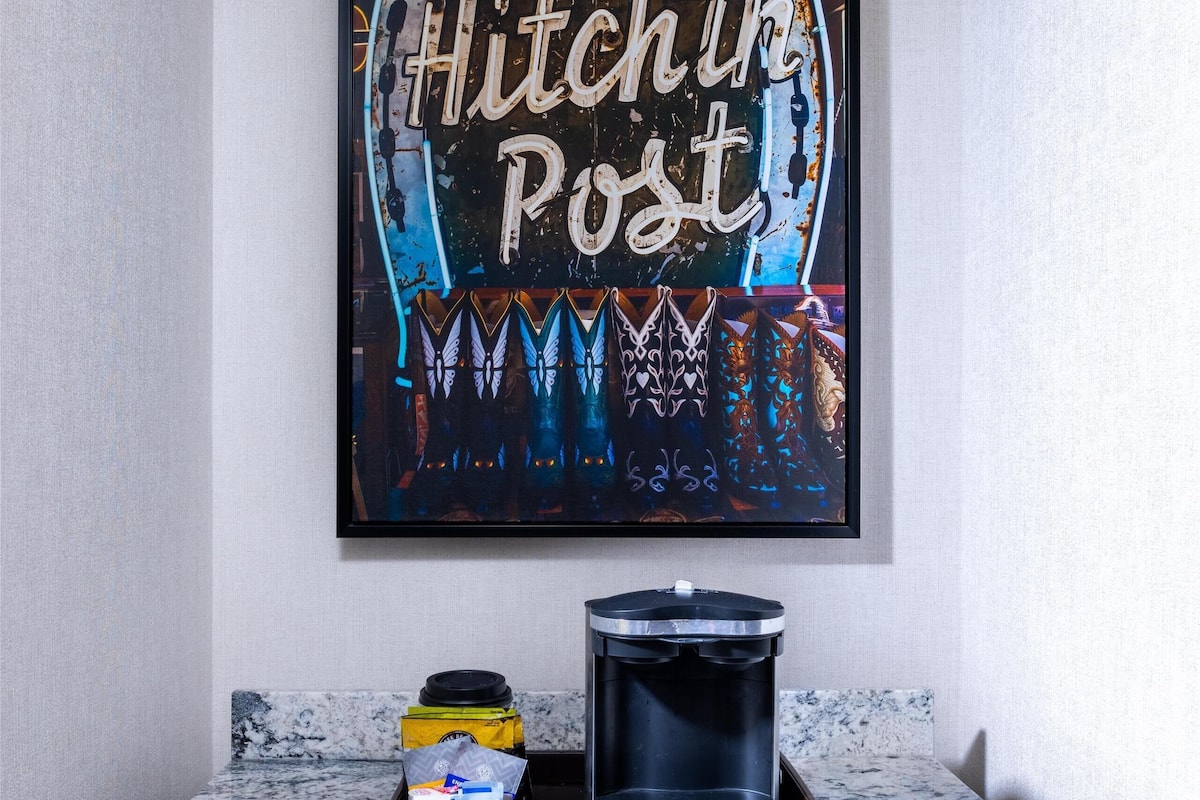 A kitchen with a marble countertop, a coffee maker, and a framed artwork on the wall.