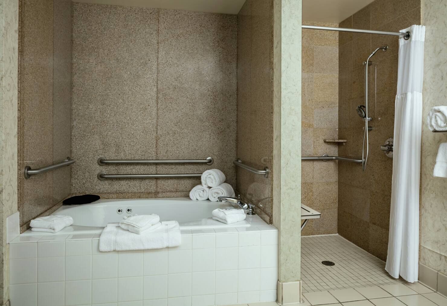 A bathroom with a bathtub, a shower, and handrails.