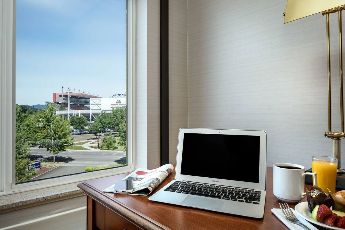 Hotelkamer met een laptop op een bureau, een koffiekop, een glas sinaasappelsap en een bord eten.