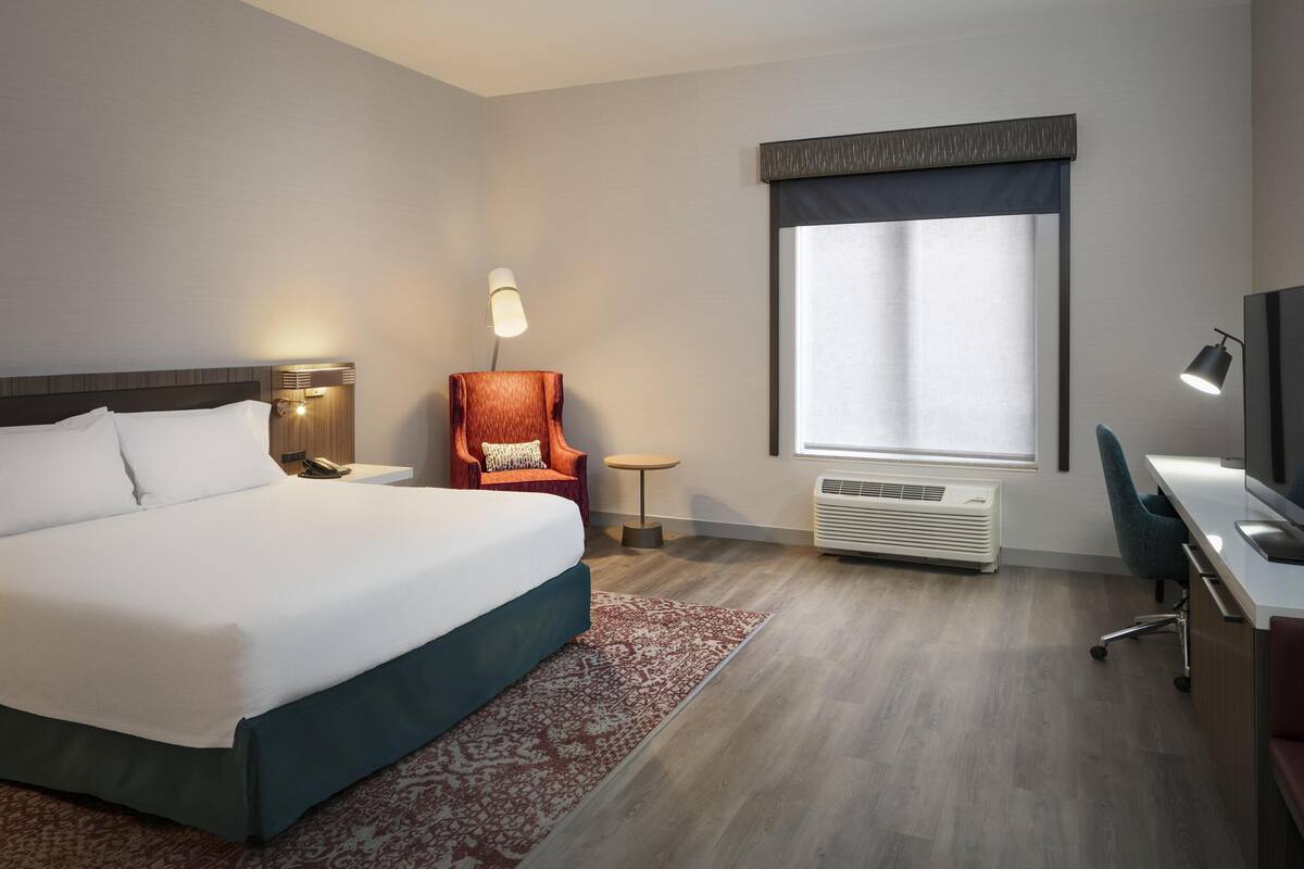 Een hotelkamer met een groot bed, een bureau, een stoel, een lamp en een raam met gordijnen.