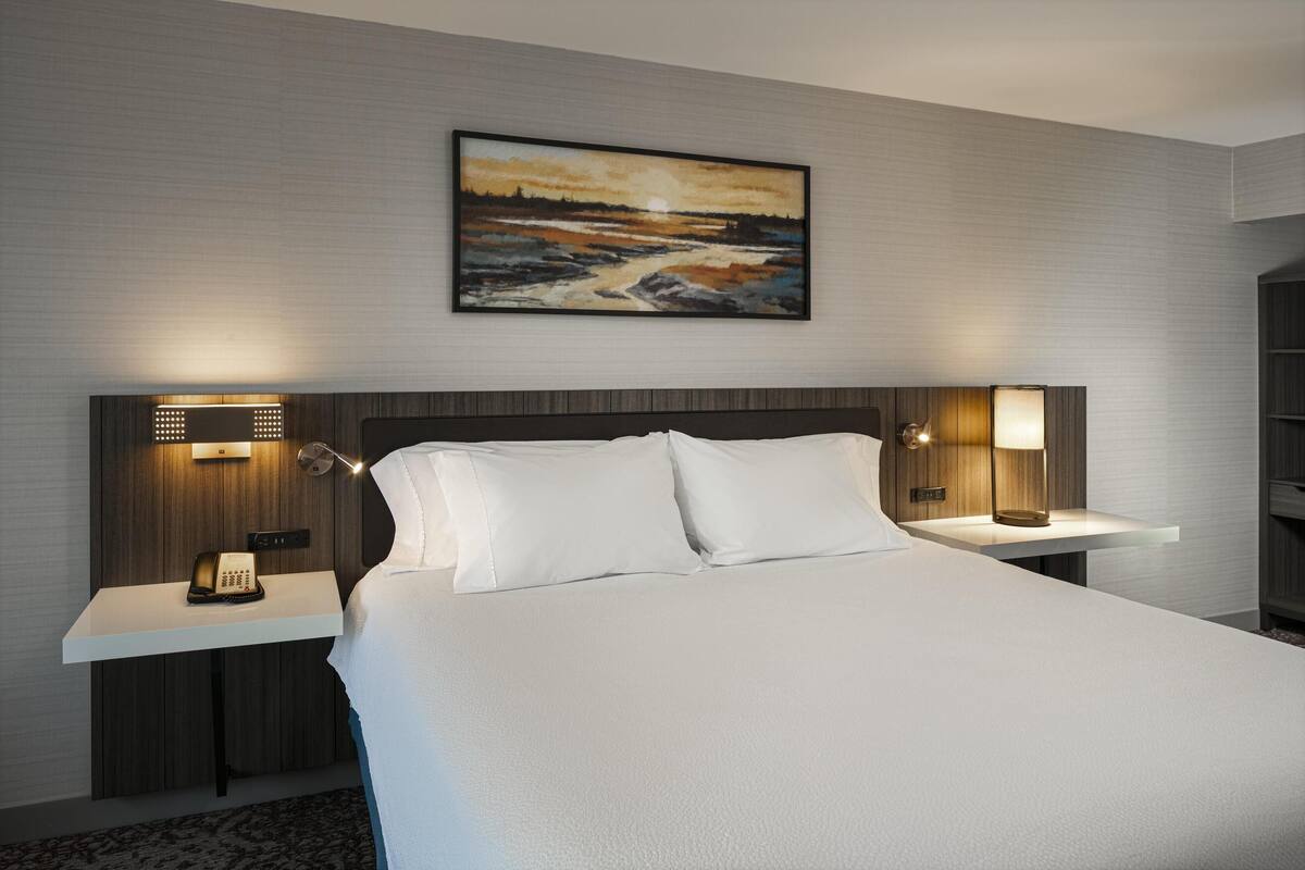 Een moderne hotelkamer met een groot bed, twee nachtkastjes met lampen, een schilderij aan de muur en een telefoon op het linker nachtkastje.