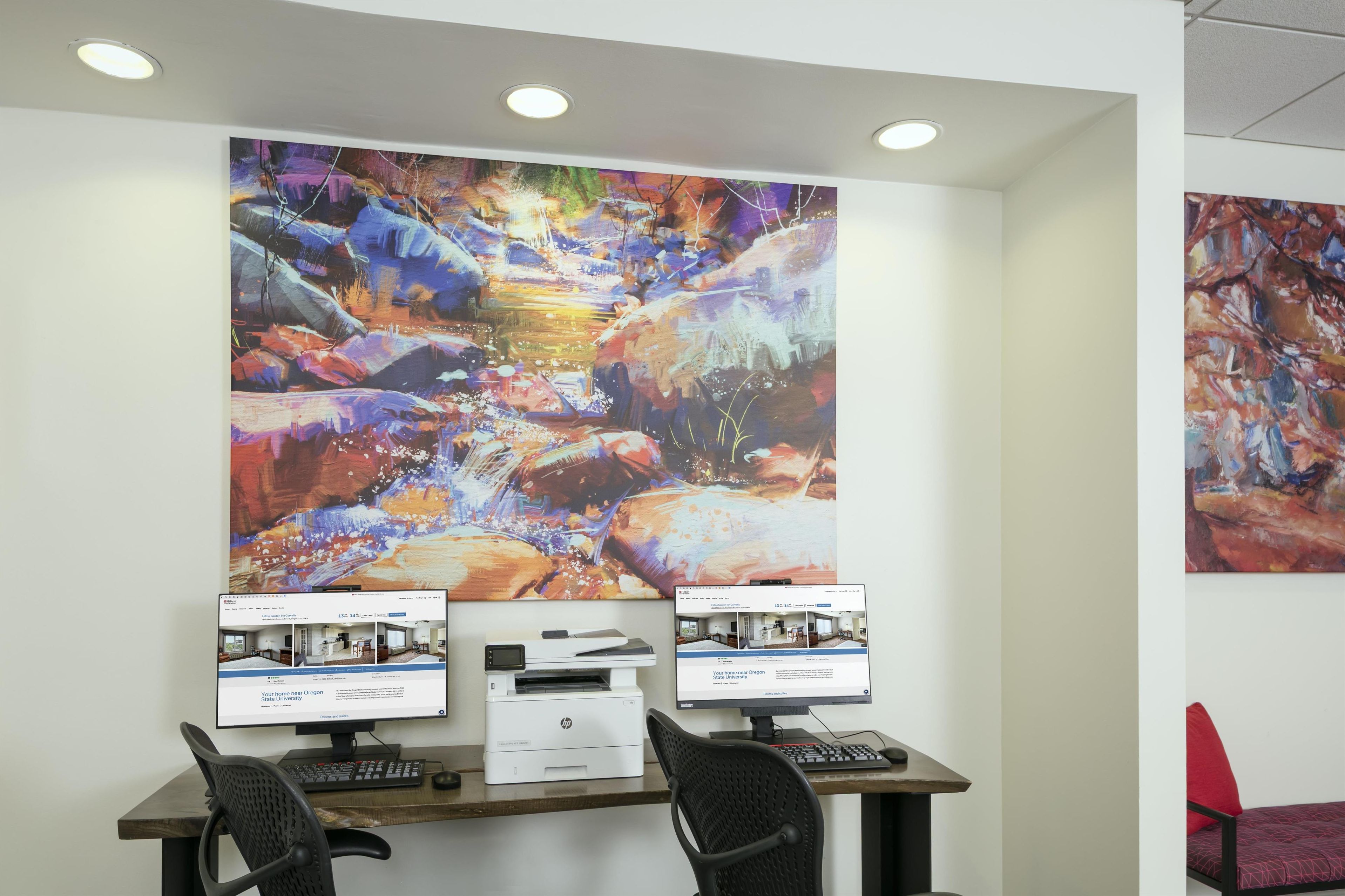 A workspace with two monitors, a printer, and a chair.