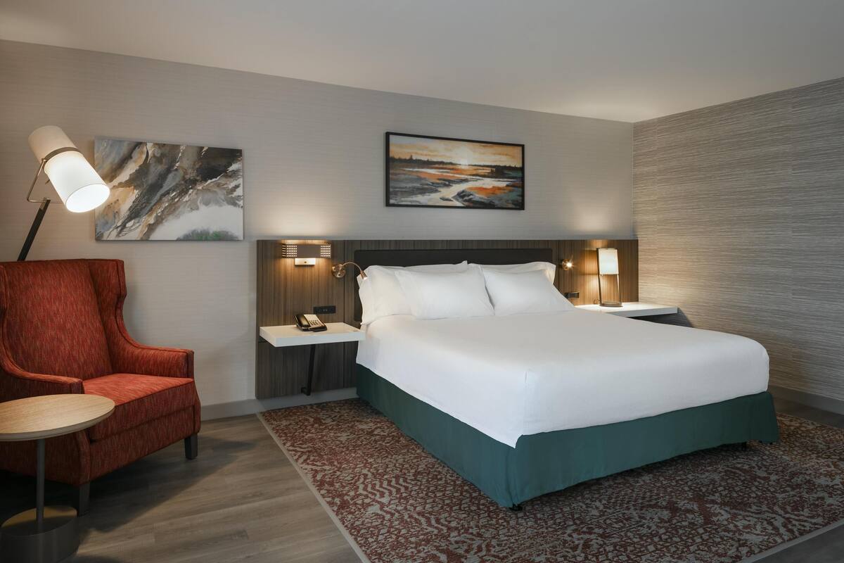 Een hotelkamer met een groot bed, een rode fauteuil, een kleine tafel en twee bedlampjes.