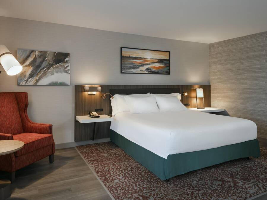A hotel room with a large bed, a red armchair, a small table, and two bedside lamps.