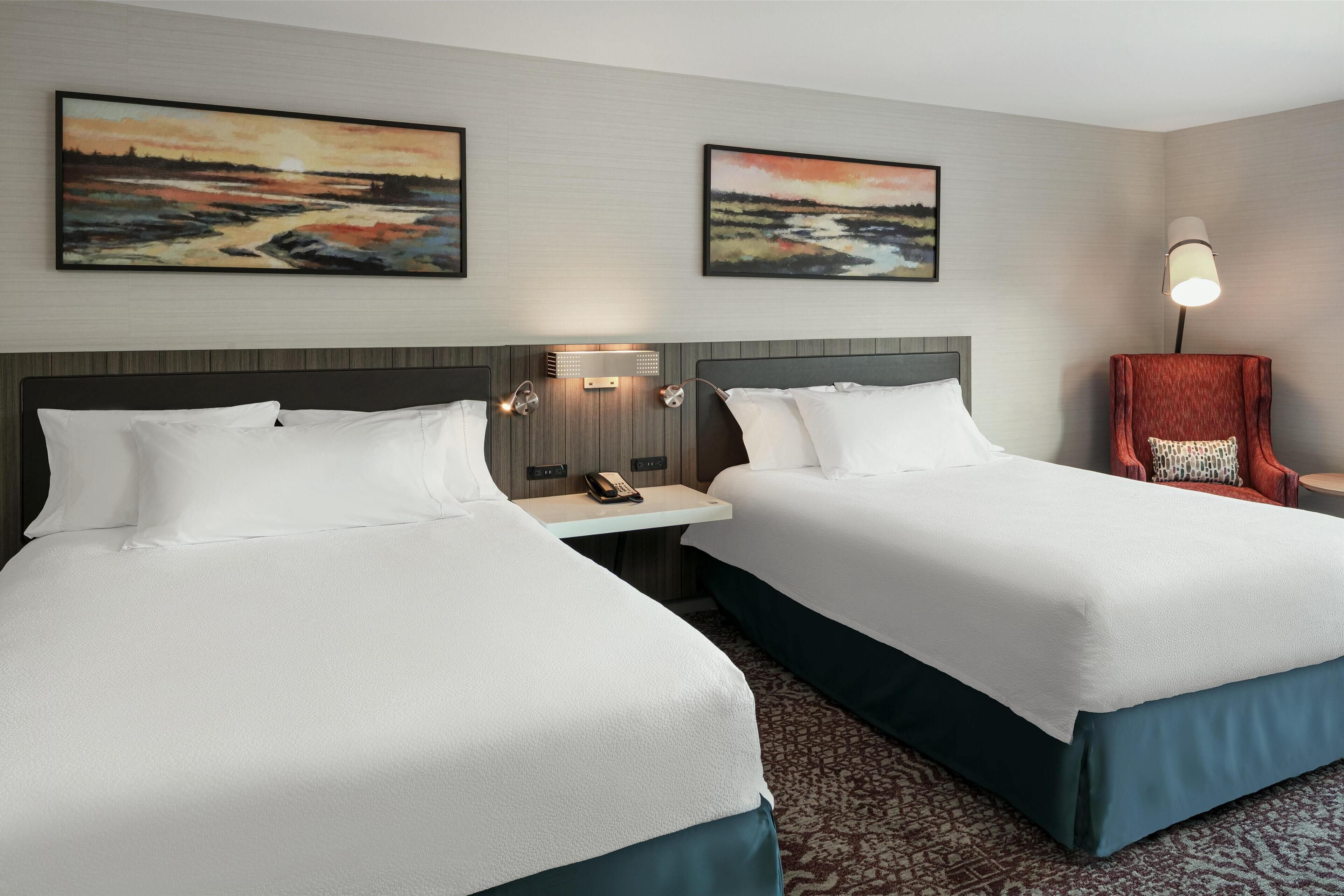 Ein Hotelzimmer mit zwei Betten, einem Nachttisch mit Lampe und zwei Bildern an der Wand.