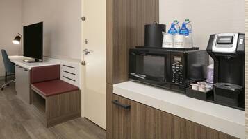 Una kitchenette compacta con microondas, cafetera y botellas de agua.