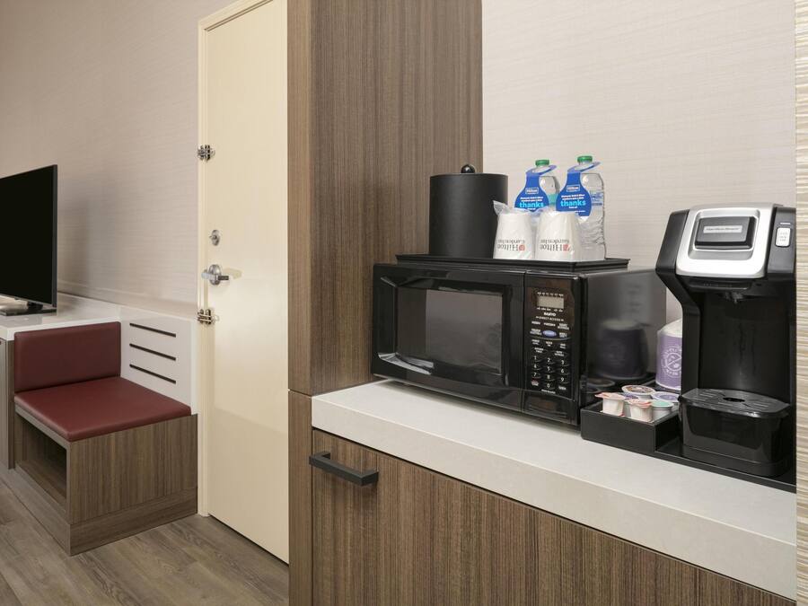 Una kitchenette compacta con microondas, cafetera y botellas de agua.