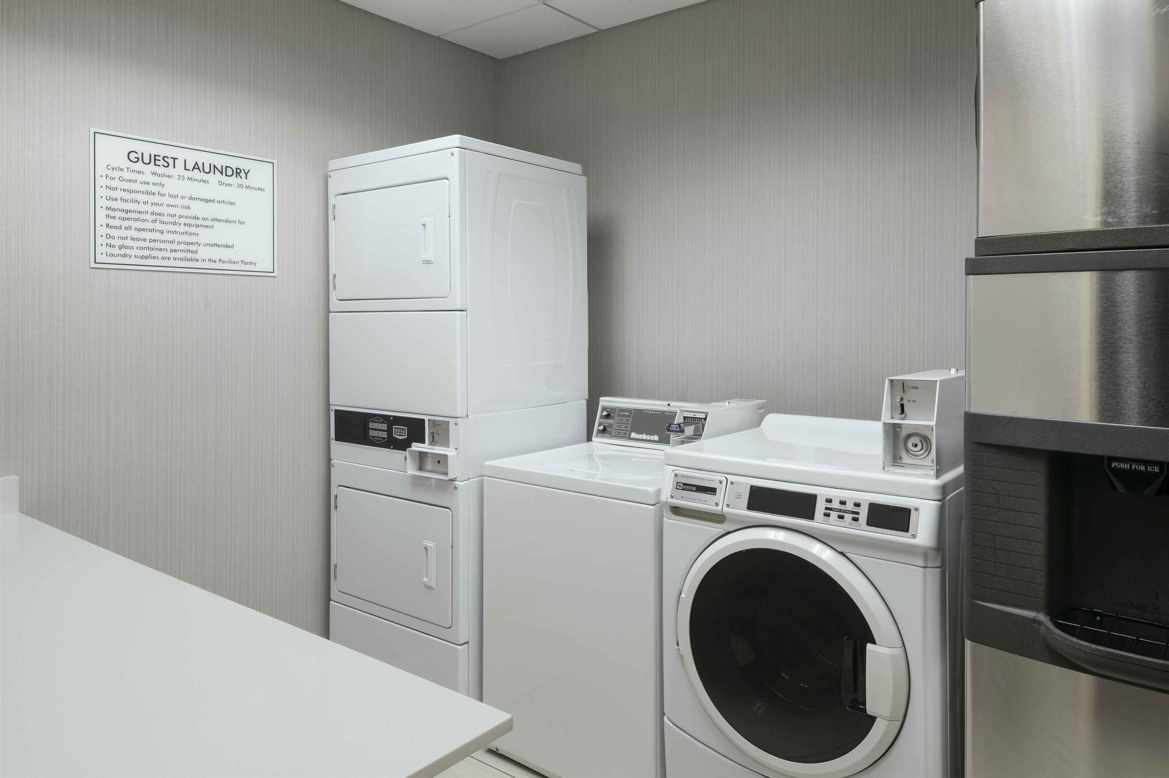 A laundry facility with a stacked washer and dryer, a front-loading washing machine, and a stainless steel refrigerator.
