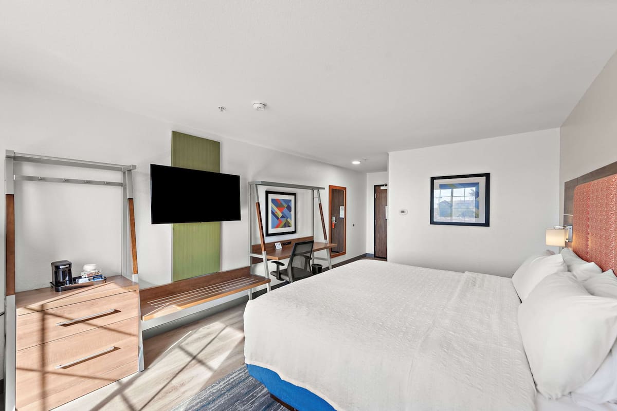 A hotel room with a bed, a desk, a chair, a television, and a door.