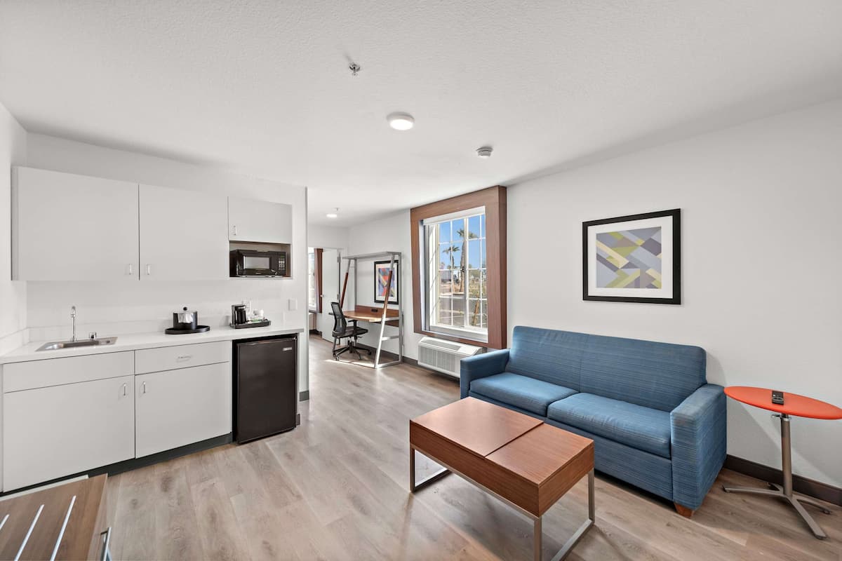 A modern kitchen with white cabinets, a black refrigerator, and a dining area with a blue sofa and a small orange table.