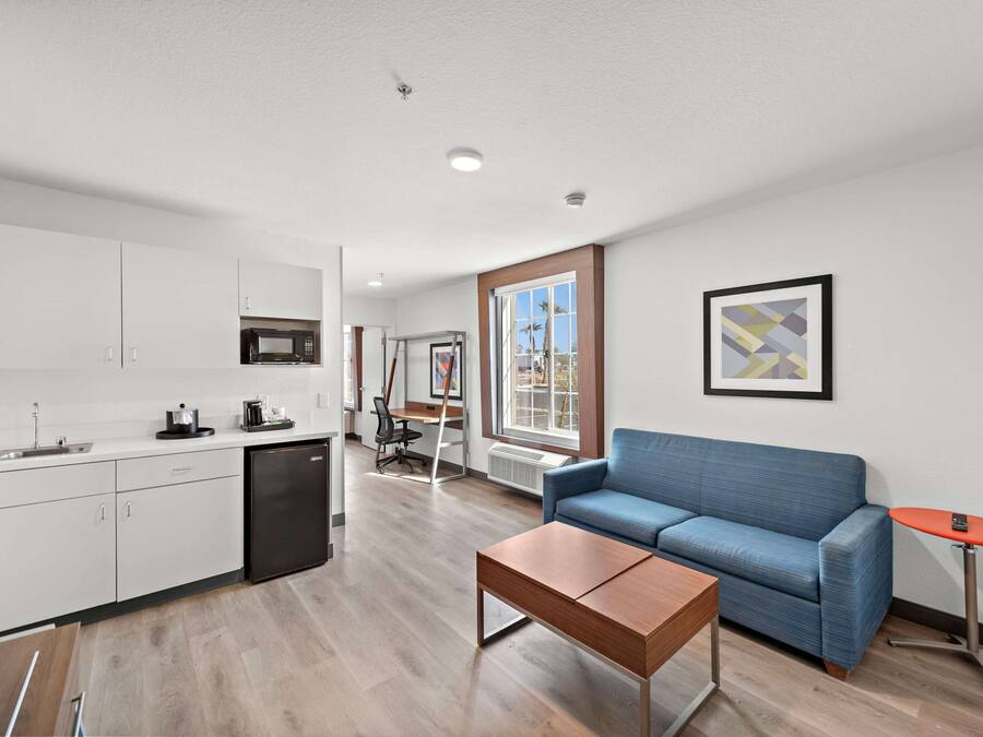 A modern kitchen with white cabinets, a black refrigerator, and a dining area with a blue sofa and a small orange table.