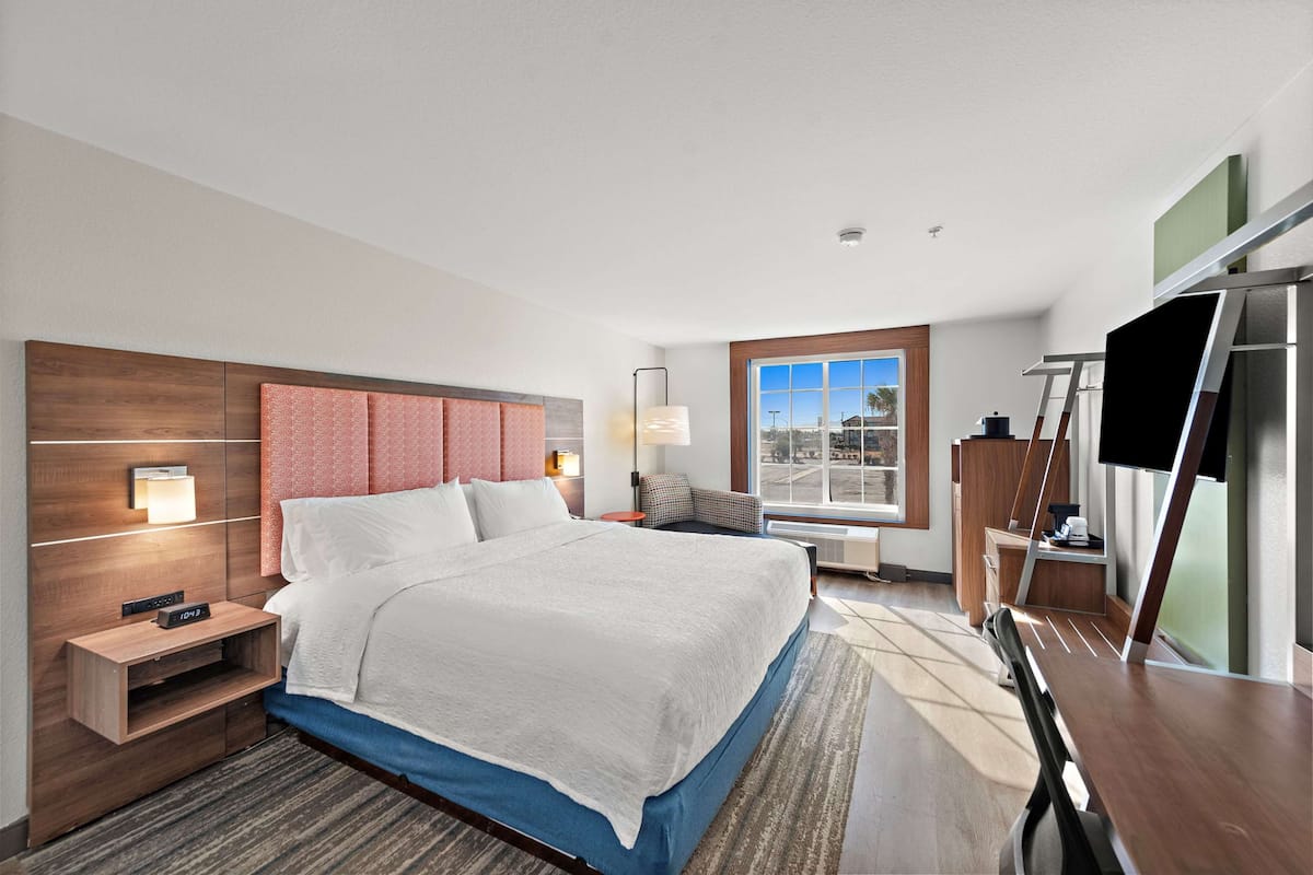 A hotel room with a large bed, bedside tables, a desk, a TV, and a window with a city view.