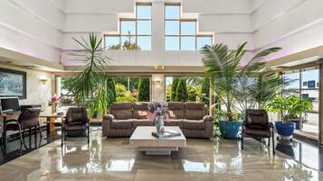 A spacious lobby with a high ceiling, a central seating area with a sofa and chairs, and large windows offering views of the outdoors.