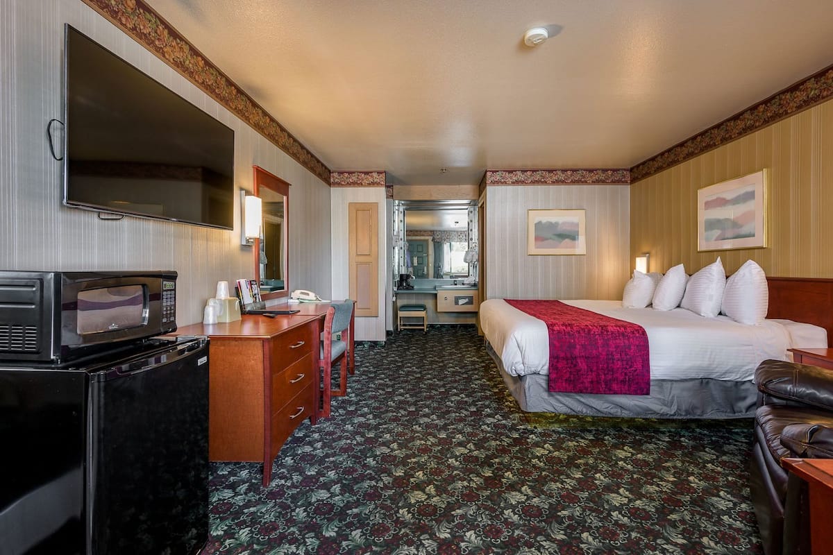 Une chambre d’hôtel avec un lit, un bureau doté d’un micro-ondes, une commode, un miroir et une salle de bain visible à travers une porte ouverte.