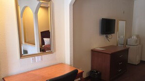 A hotel room with a wooden desk, a chair, a mirror, a television, a dresser, and a trash can. - Scottish Inn & Suites (Houston)