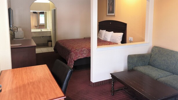 A hotel room with a bed, a desk, a chair, a sofa, and an arched doorway leading to a bathroom. - Scottish Inn & Suites (Houston)