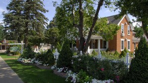 Una casa de ladrillo con cerca blanca de piquetes, rodeada de jardines cuidados y una acera.