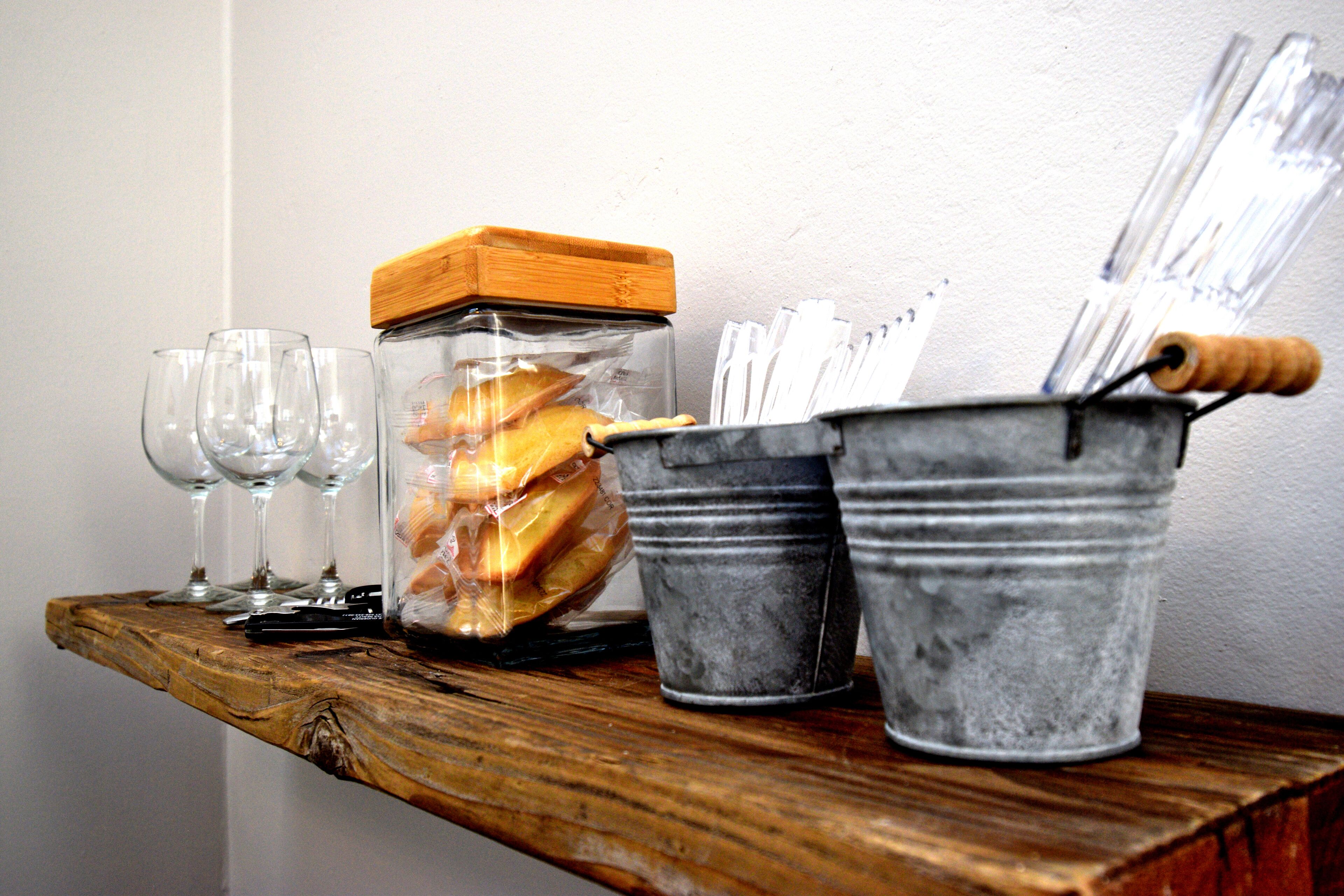 A wooden shelf with a glass jar containing cookies, a metal bucket with utensils, and empty wine glasses.