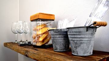 A wooden shelf with a glass jar containing cookies, a metal bucket with utensils, and empty wine glasses.