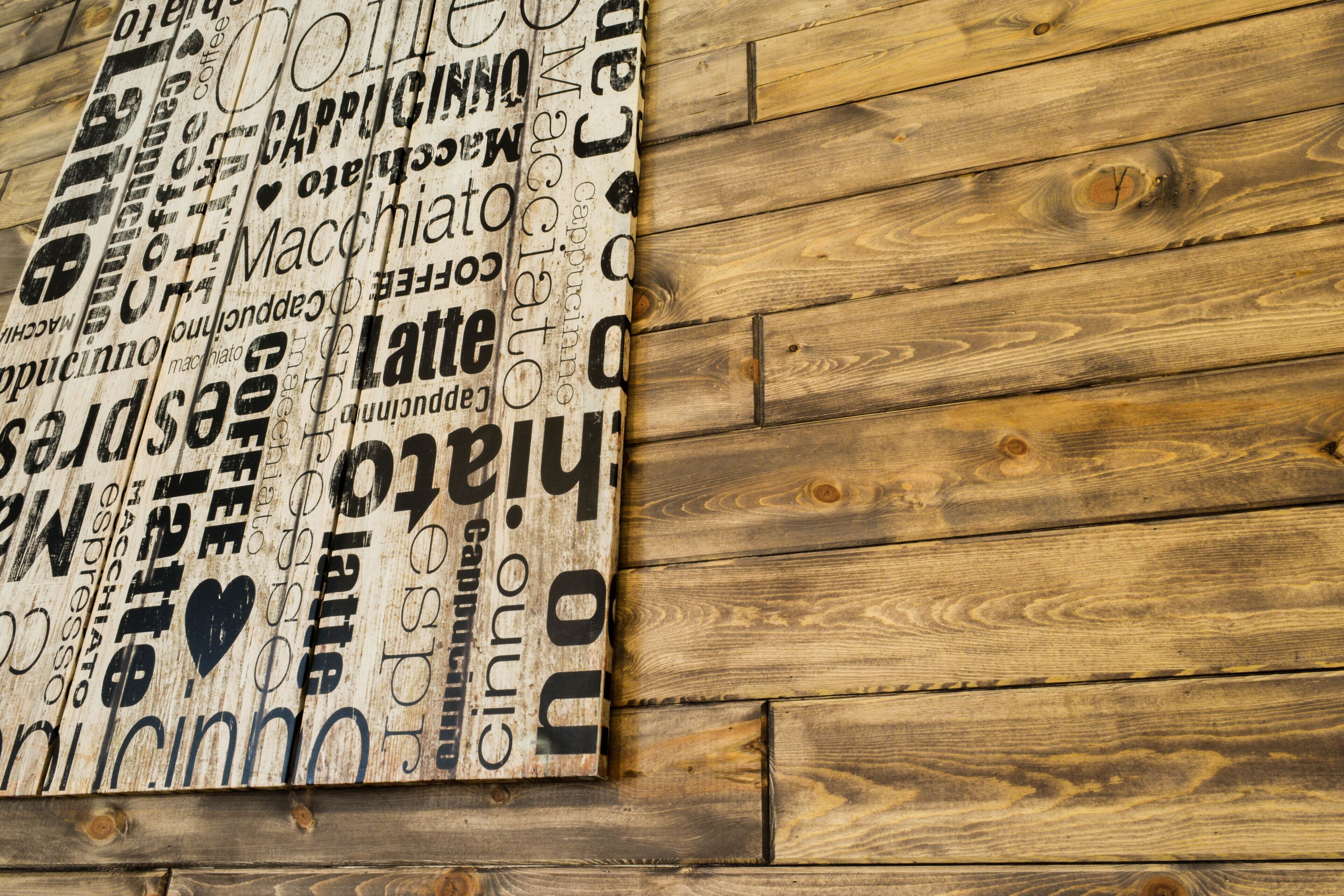 Een houten wand met een bord waarop verschillende woorden en uitdrukkingen over koffie staan.