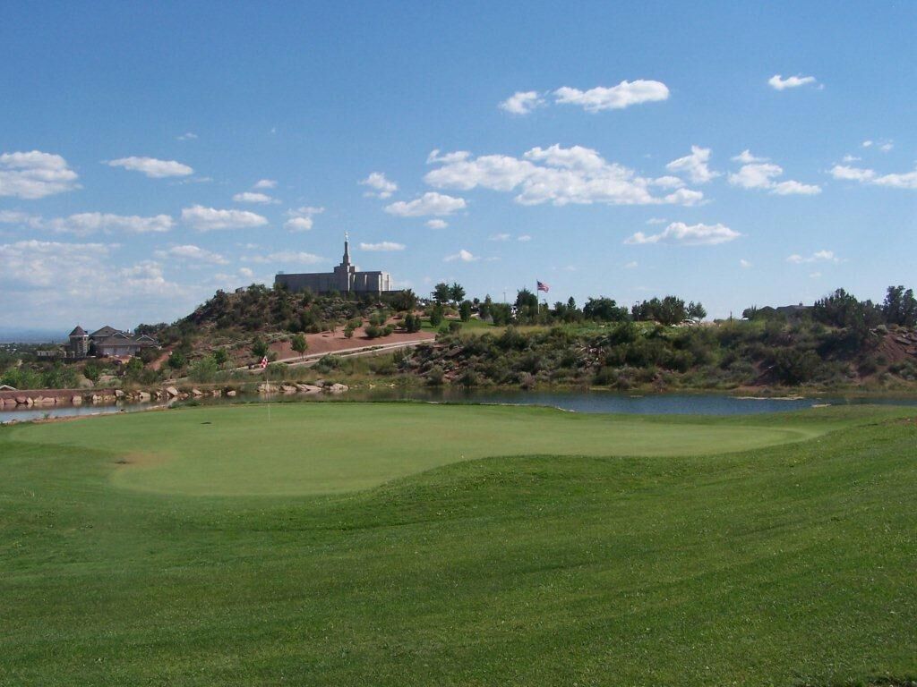 A golf course with a water body, a flag, and a building in the background.