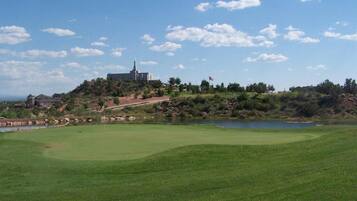 A golf course with a water body, a flag, and a building in the background.