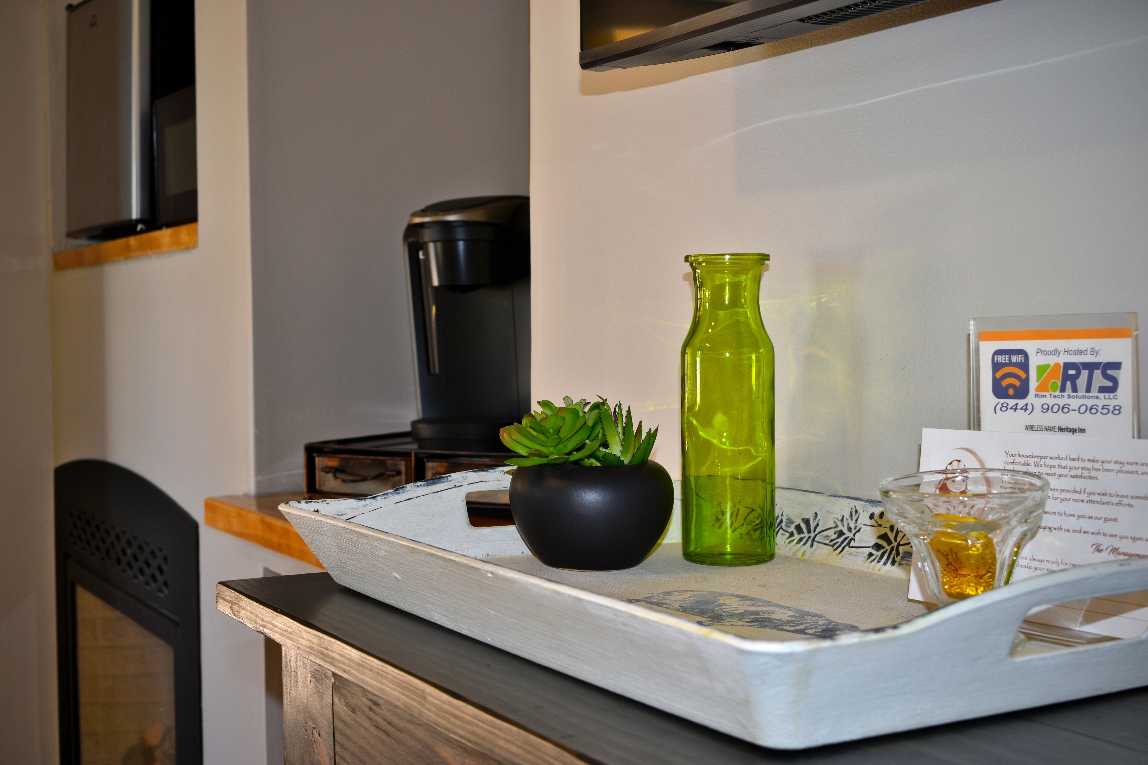 A tray with a black bowl, a green vase, and a glass with a yellow liquid on a wooden table.