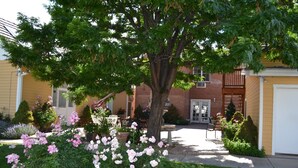 Edificio residencial con un jardín cuidado que presenta flores rosadas y un árbol grande.