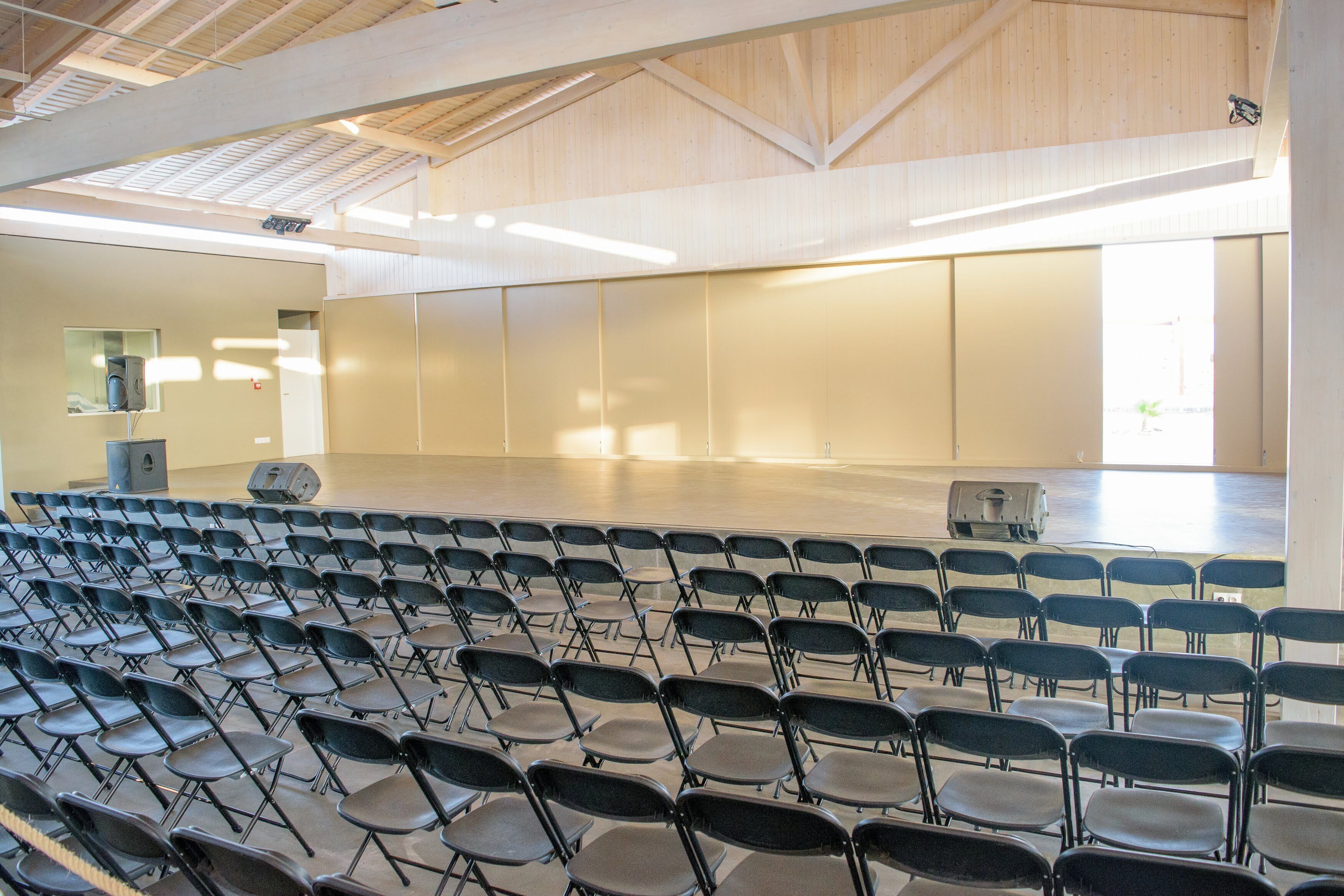 Une salle de conférence avec des rangées de chaises, un projecteur et une grande fenêtre.