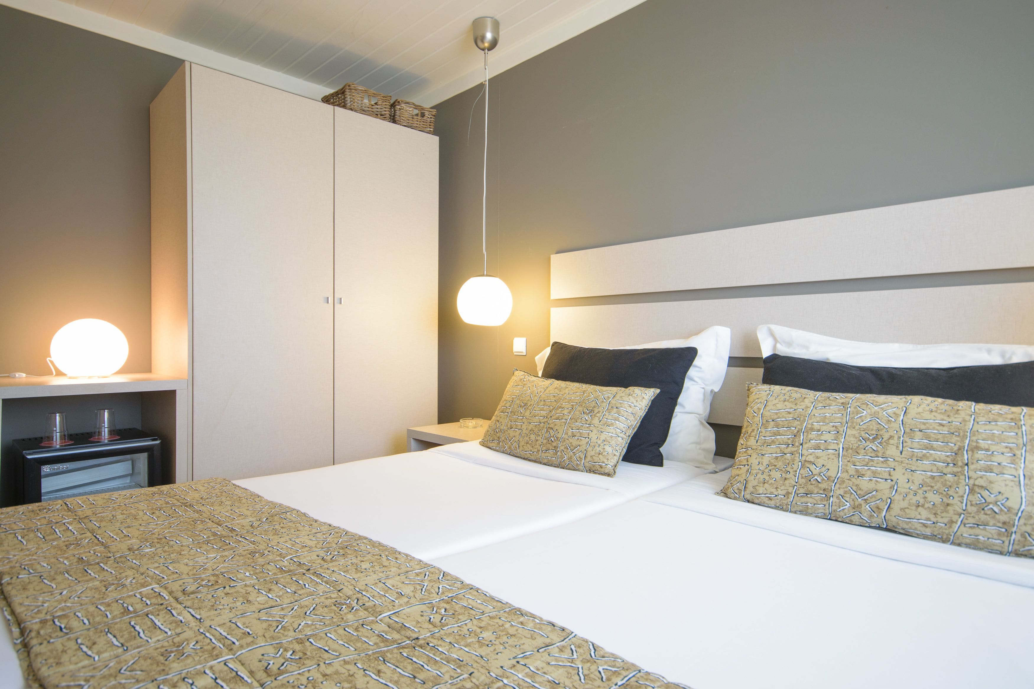 A neatly arranged hotel room with a large bed, two bedside tables, a wardrobe, and a wall-mounted lamp.