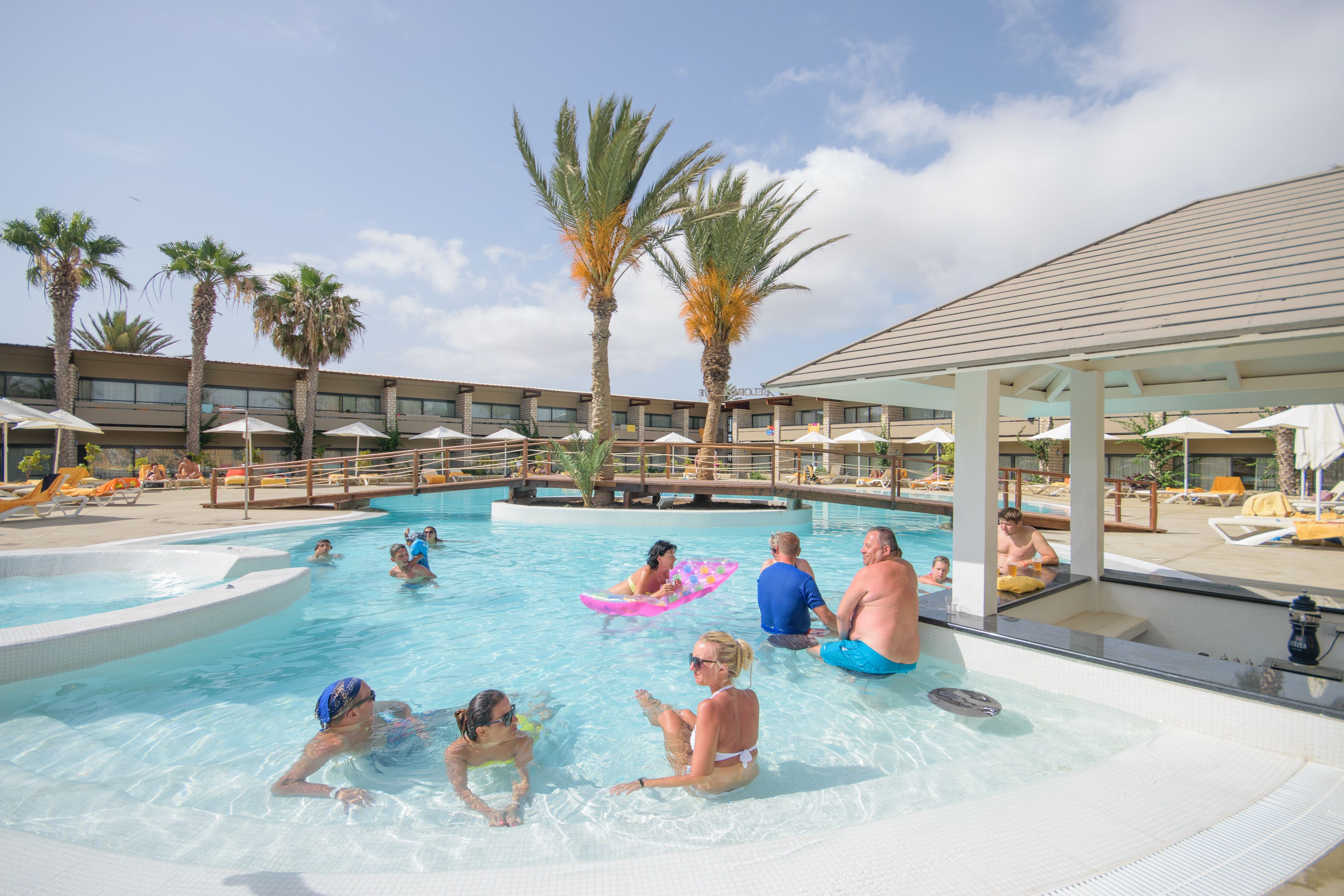 Zona de piscina con sillones de descanso y palmeras.