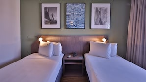 Een hotelkamer met twee bedden, een nachtkastje met een lamp en drie ingelijste foto’s aan de muur.