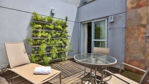 Een balkon met een glazen tafel en stoelen, een comfortabele lounge fauteuil en een verticale tuin.
