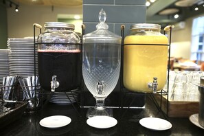 Uma estação de bebidas com três dosadores, cada um com uma torneira e um bico, além de um conjunto de pratos e utensílios empilhados.