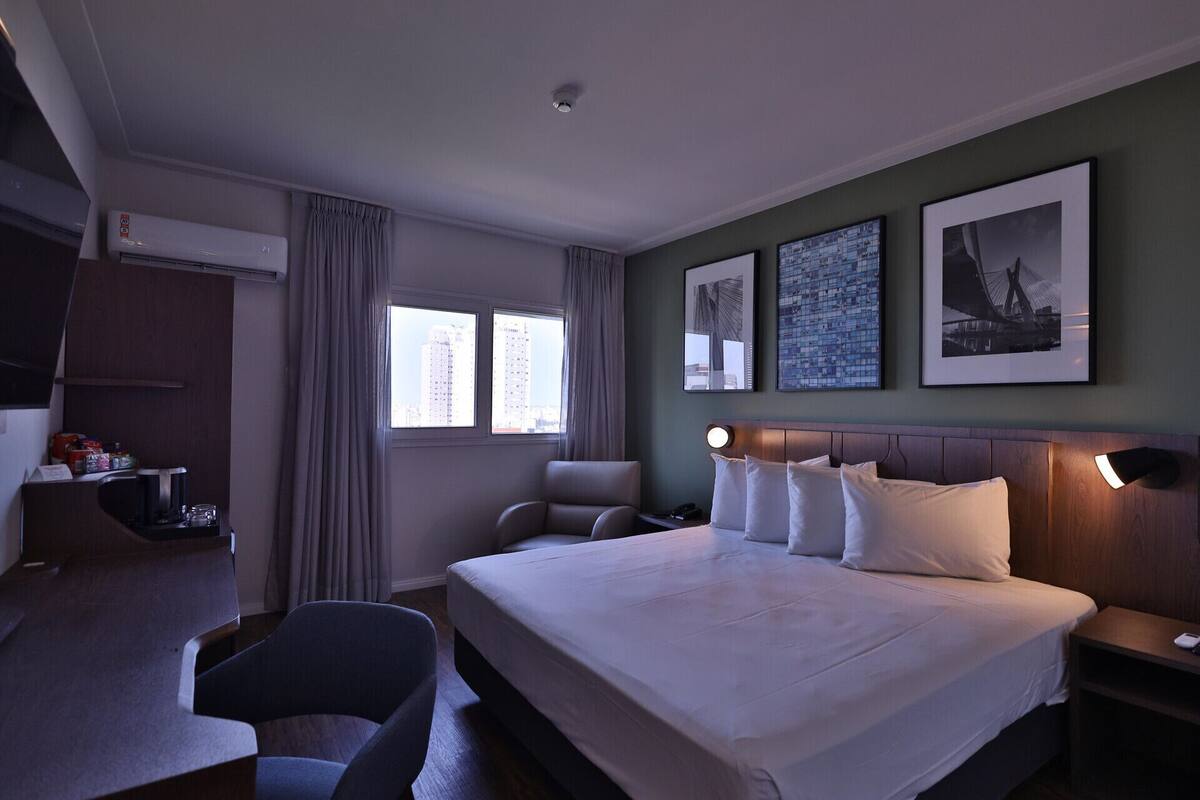 Une chambre d’hôtel avec un lit, un bureau, une chaise et deux fenêtres.