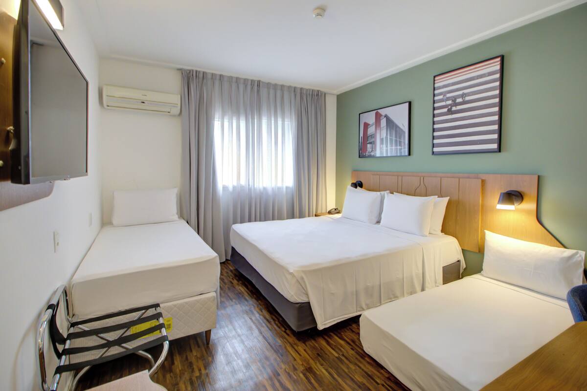 Une chambre d’hôtel avec deux lits simples, un lit double, une télévision, un climatiseur et une fenêtre avec des rideaux.