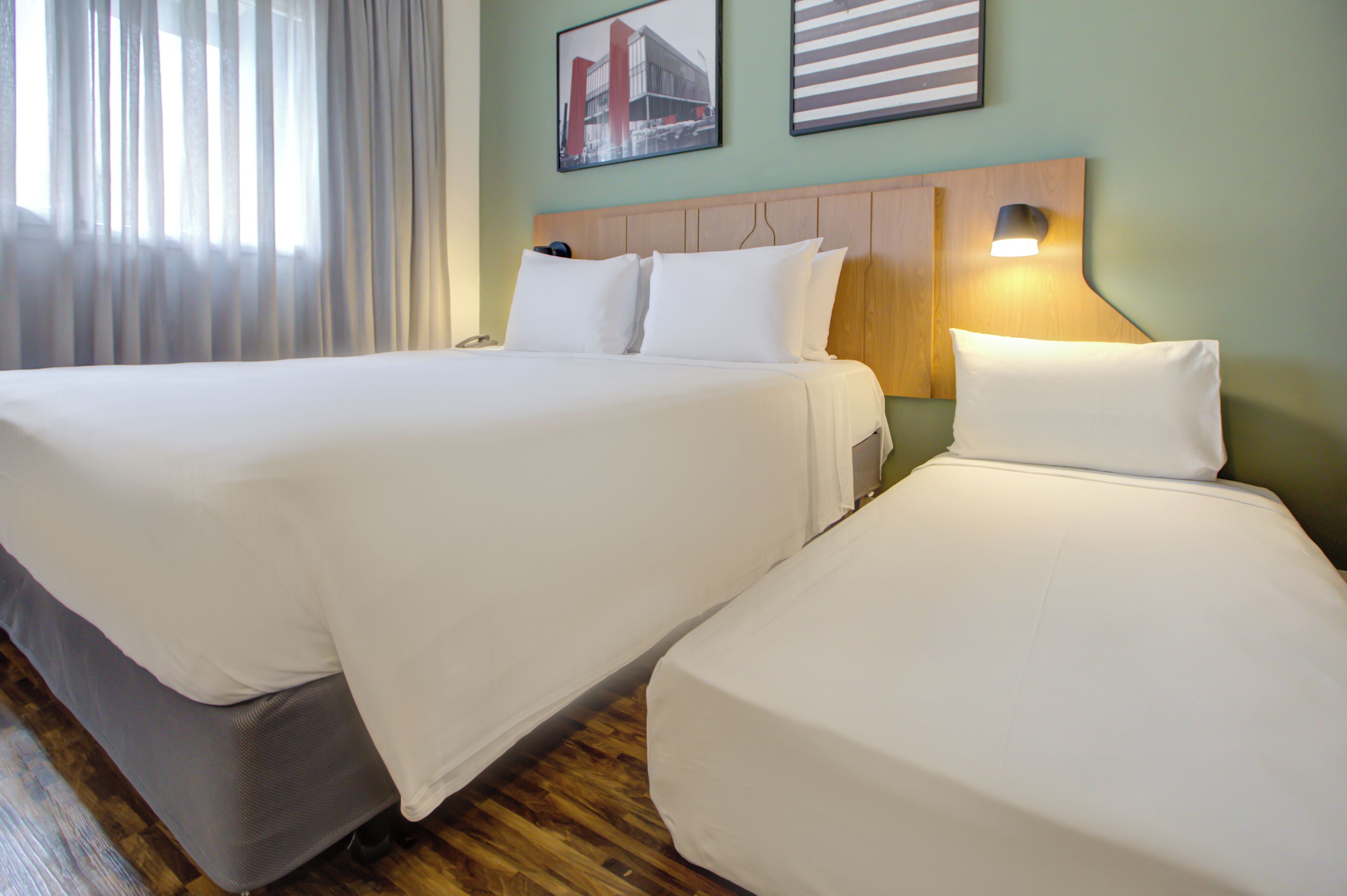Ein Hotelzimmer mit zwei Betten, einem Holzkopfende, einem Nachttisch und einem Fenster mit Vorhängen.