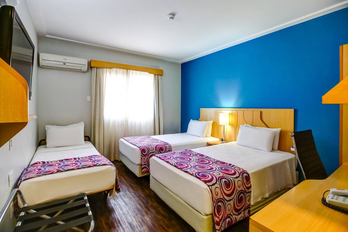 Une chambre d’hôtel avec deux lits, un bureau, une chaise, une lampe et un appareil de climatisation.