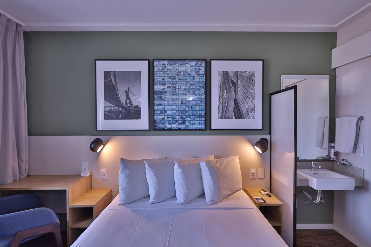 Une chambre d’hôtel comprenant un lit, des tables de chevet, un bureau et une salle de bain avec un lavabo et un miroir.