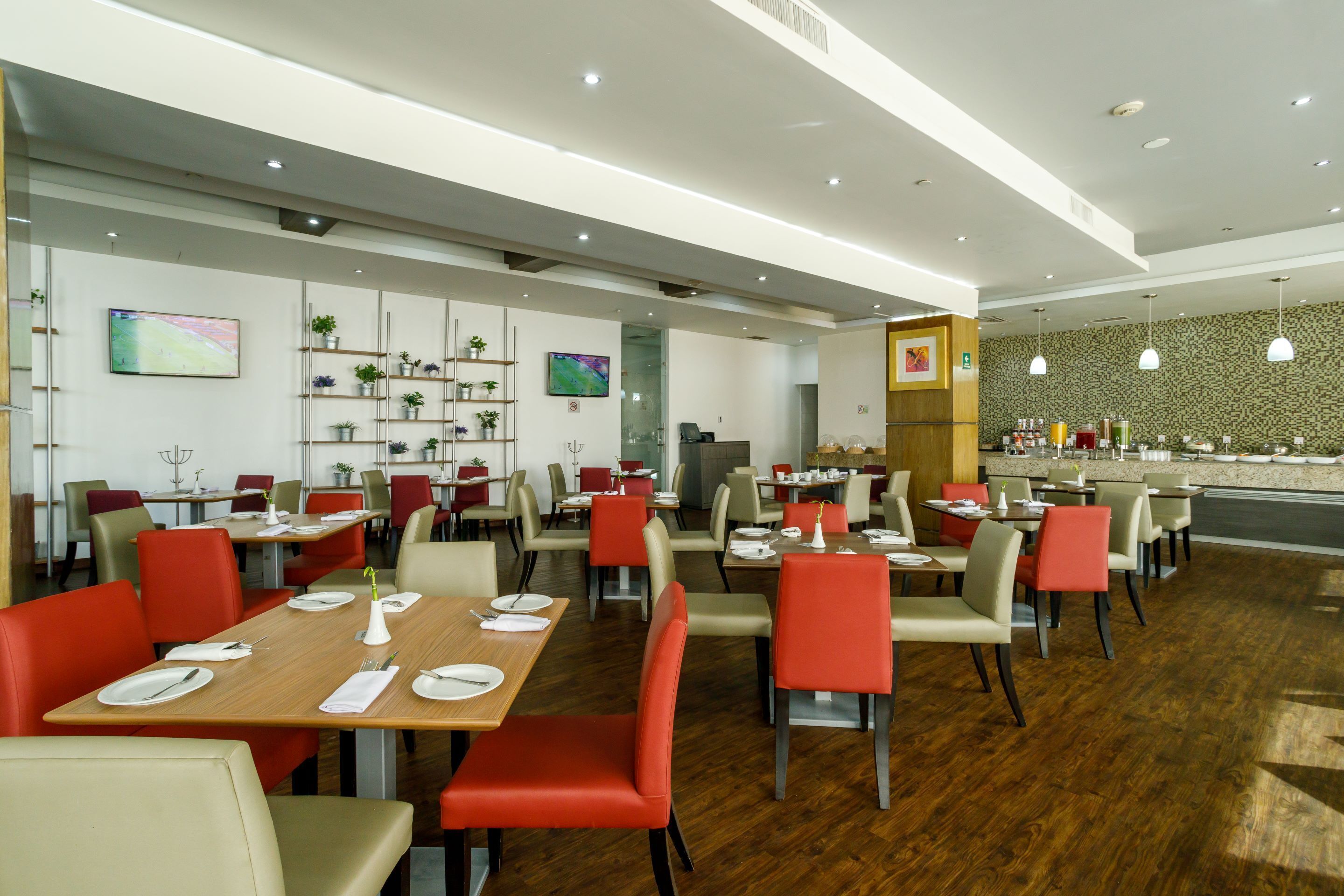 A modern restaurant with wooden tables and red chairs, a bar area, and a patterned wall.