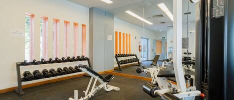 A gym with exercise equipment, dumbbells, and benches.
