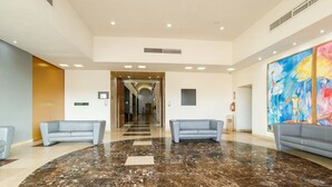 A spacious lobby with a polished marble floor, two sofas, a large abstract painting, and a clear view into the hallway.