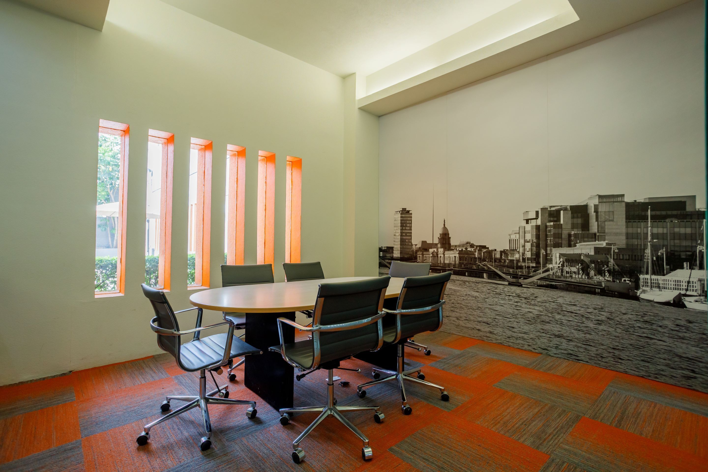 A conference room with a round table, four chairs, and a cityscape mural on the wall.