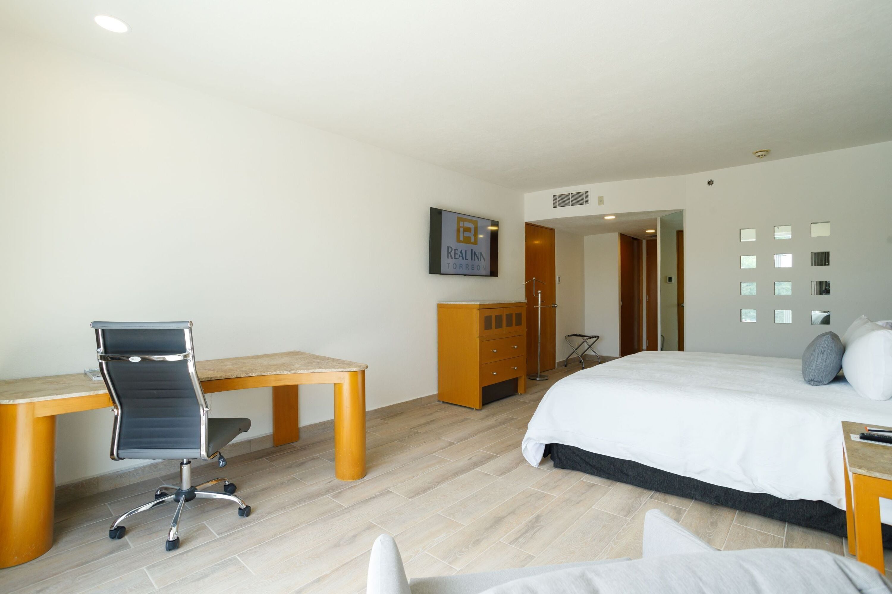 Een hotelkamer met een bed, een bureau, een stoel, een kledingkast en een televisie aan de muur.